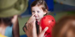 Ein lächelndes Mädchen greift sich an die Nase.