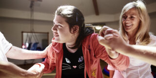 Eine junge Frau mit Behinderung genießt Bewegung - mit Unterstützung mehrerer helfender Hände.