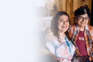 Zwei Frauen umarmen sich herzlich und lächeln in die Kamera.