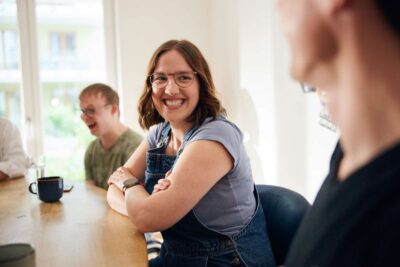 Junge Frau sitzt in einer Gruppe am Tisch, engagiert und lachend.