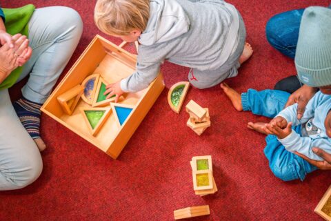 Kinder sitzen am Boden und spielen mit Holzbausteinen.