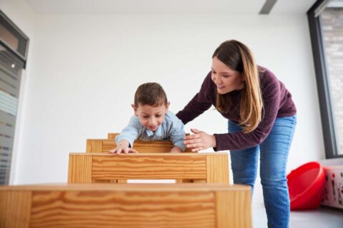 Eine junge Frau beugt sich zu einem Jungen, der klettert und spielt.