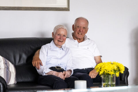 Monika Niemann und Uwe Bartel sind von Düsseldorf in die Wagnerstraße gezogen. Sie sitzen auf ihrem Sofa und lächeln in die Kamera.