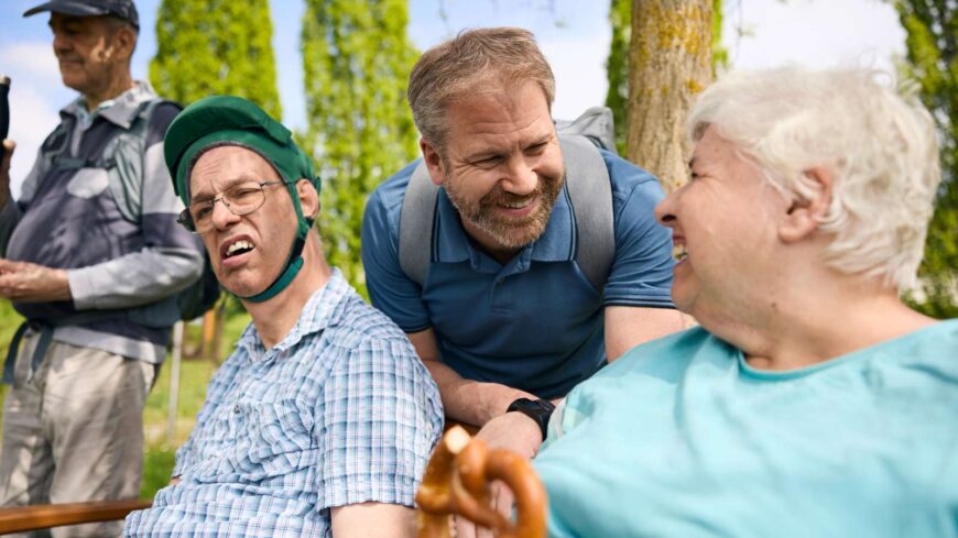 Menschen mit und ohne Behinderung sind als Gruppe unterwegs, lachen gemeinsam.