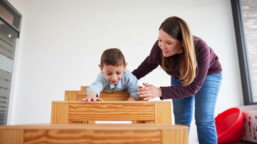 Eine junge Frau beugt sich zu einem Jungen, der klettert und spielt.