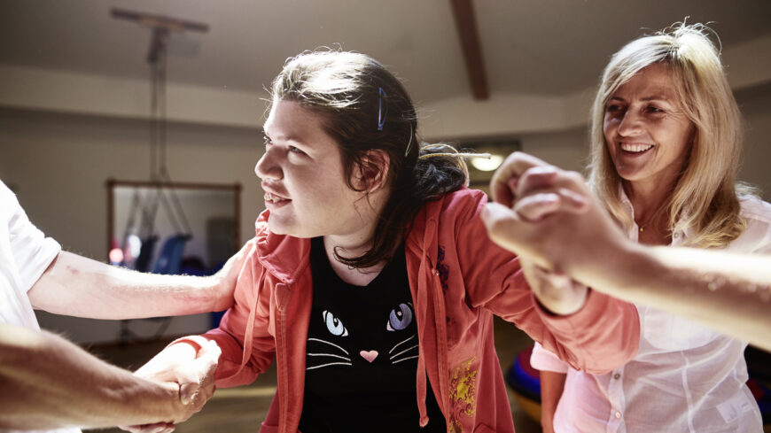 Eine junge Frau mit Behinderung genießt Bewegung - mit Unterstützung mehrerer helfender Hände.